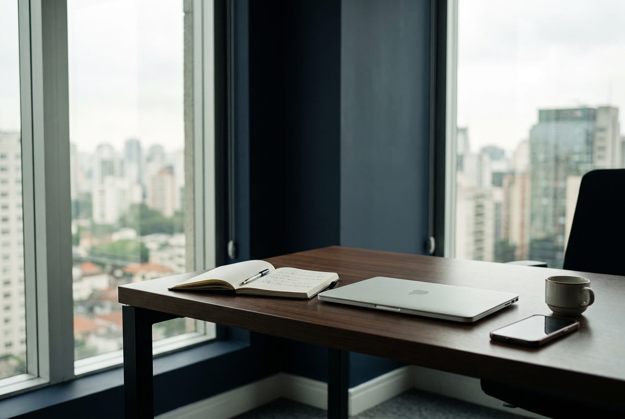 Mesa de trabalho com caderno de anotações, de frente para prédios de São Paulo.